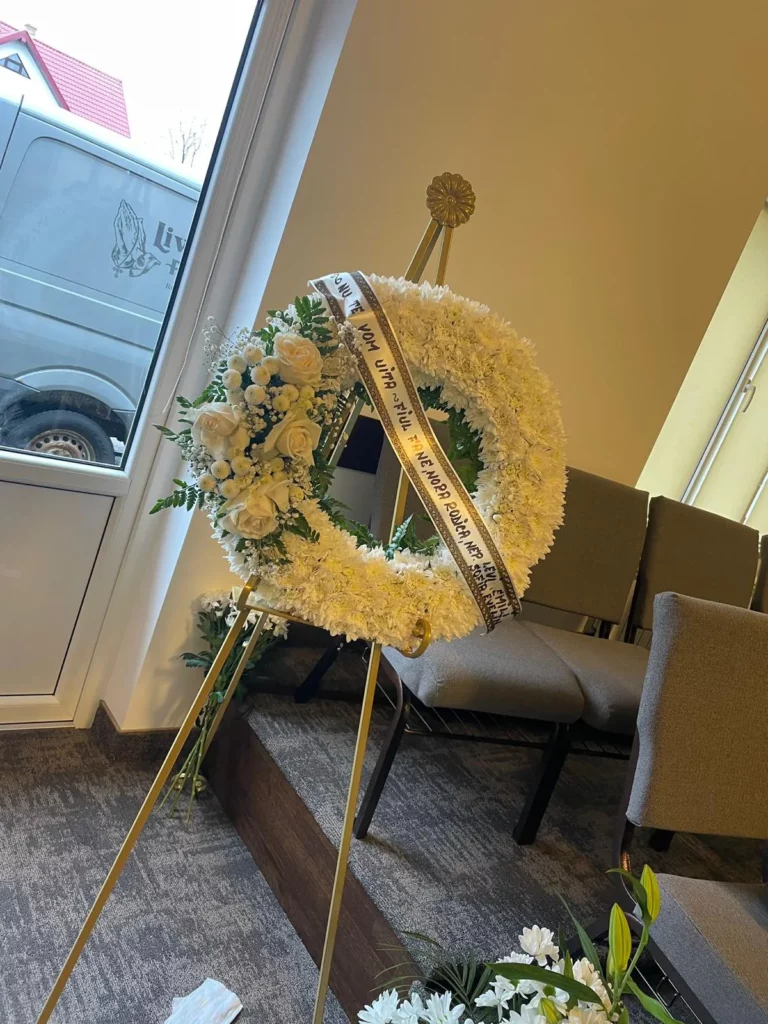 Coroană funerară din flori naturale albe, pe suport, pregătită pentru ceremonie